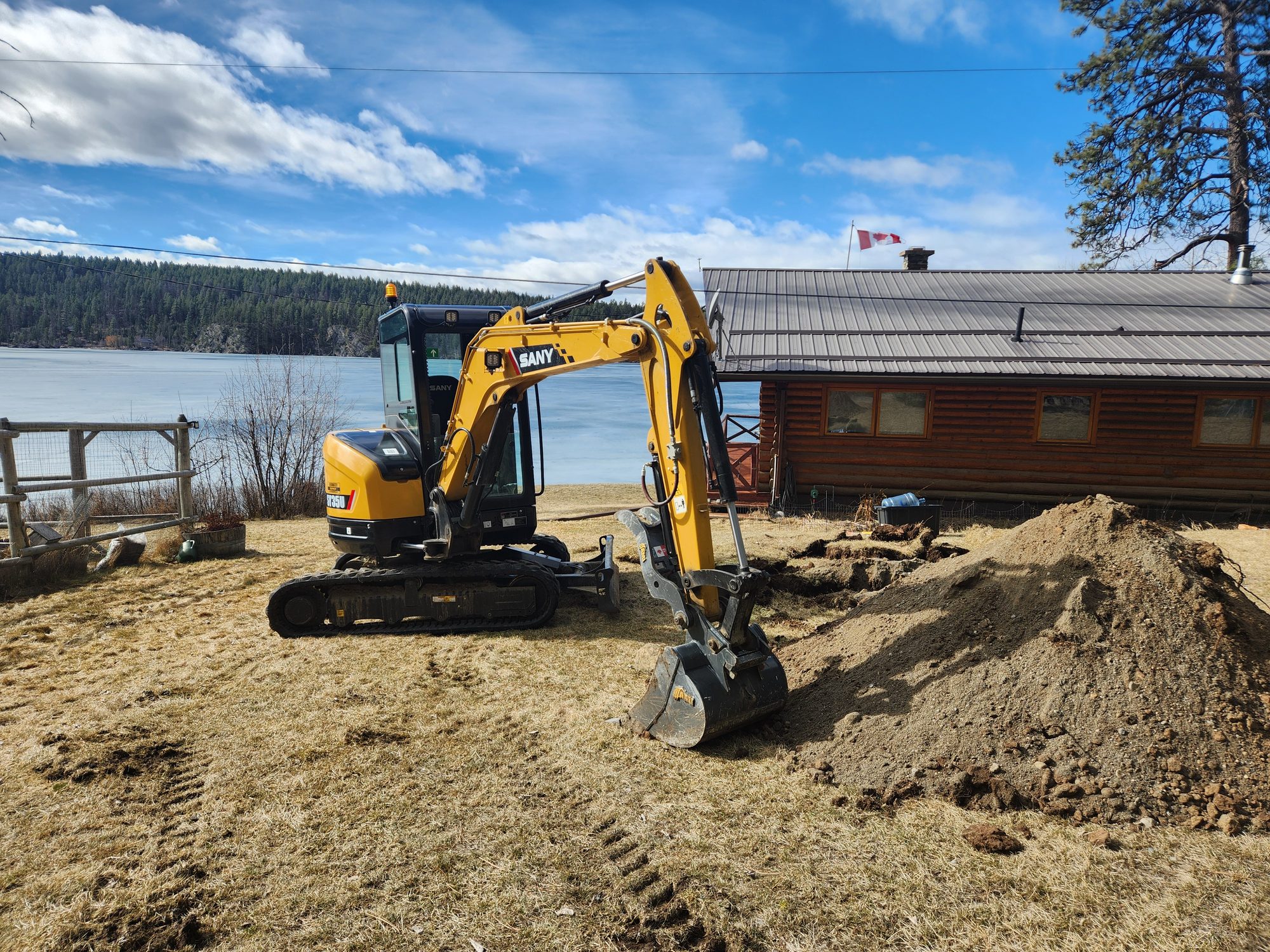 Excavator working on a lakeside septic system beside a log home