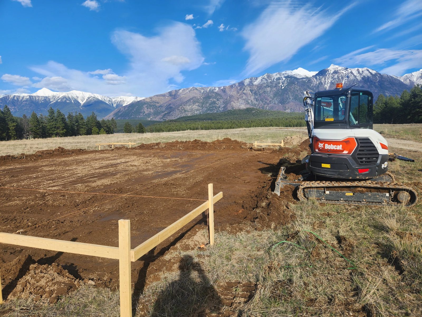 Excavator preparing a staked septic bed with the Rockies behind